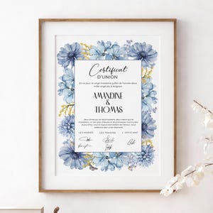 Könnte beinhalten: Eine gerahmte Hochzeitsurkunde mit dem Titel Certificat d'Union und den Namen Amandine und Thomas. Das Dokument ist mit einem Rand aus blauen Aquarellblumen und gelben Zweigen verziert und enthält gedruckten Text sowie Unterschriftszeilen für das Paar.
