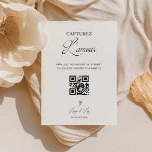 Peut inclure: Une carte blanche avec du texte noir qui dit "Capturez L'amour" et un code QR. Le texte sous le code QR dit "Partagez vos photos avec nous! Scannez et ajoutez vos photos." Sous le texte se trouve un symbole de cœur et le texte "Louise & Loo 26 Juillet 2030."