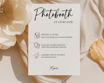 May include: A rectangular white sign with black text and icons. The header reads Photobooth ET LIVRE D'OR. Below are three sections with icons: a camera for PRENEZ LA POSE, two photos for COLLEZ VOTRE PHOTO, and a pen for LAISSEZ-NOUS UN MOT. Merci is at the bottom.
