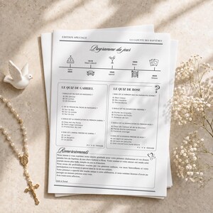 May include: A white paper program titled Edition Speciale La Gazette des Baptemes featuring a timeline of events, two quizzes for Gabriel and Rose, and a thank you note, accompanied by a white ceramic dove and a string of white pearl beads.