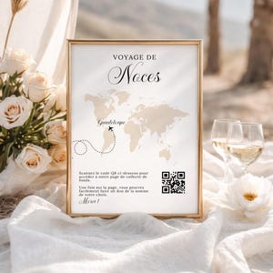 May include: A framed sign with the words "VOYAGE DE Noces" and a world map with a highlighted route to Guadeloupe. The sign includes a QR code and French text. The sign is surrounded by flowers and glasses of wine.