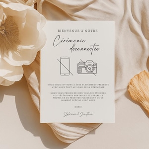 Peut inclure: Une pancarte blanche avec du texte noir et des icônes qui dit "Bienvenue à notre cérémonie déconnectée". La pancarte présente un téléphone barré et un appareil photo barré. Le texte sous les icônes dit "Nous vous invitons à être pleinement présents avec nous tout au long de la cérémonie. Nous vous prions de bien vouloir éteindre vos téléphones portables et appareils photo, et de profiter pleinement de ce moment spécial avec nous. Merci, Sylviana & Jonathan."
