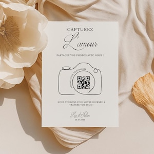Può includere: Un biglietto bianco con testo nero e un'illustrazione in bianco e nero di una macchina fotografica con un codice QR. Il testo recita "Capturez L'amour" e "Partagez vos photos avec nous!"  Il testo sotto la macchina fotografica recita "Scannez pour télécharger" e "Nous voulons voir notre journée à travers vos yeux!"  Il biglietto include anche il testo "Lisa et Julien" e "28.07.2040".
