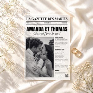 Könnte beinhalten: Eine Hochzeitszeitung mit der Überschrift "AMANDA ET THOMAS" und dem Satz "Sunissent pour la vie!". Die Zeitung zeigt ein Schwarz-Weiß-Foto eines Paares und zwei goldene Eheringe.