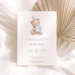 May include: A white invitation card featuring a watercolour illustration of a teddy bear wearing a blue party hat and holding a blue number one. The card includes French text, announcing a first birthday celebration for Marceau, with the date and time.