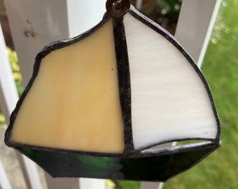 May include: A stained glass sailboat ornament with a white sail, a yellow sail, and a green hull.