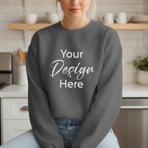 May include: A charcoal gray sweatshirt with the text "Your Design Here" in a white script font. The sweatshirt is a crew neck style and is being worn.