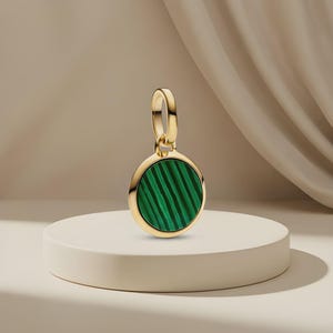 Peut inclure: Un pendentif circulaire en or doté d'une incrustation de malachite vert vif avec des motifs rayés vert foncé distincts. Le pendentif comprend une bélière en or poli sur le dessus, conçue pour être fixée à une chaîne ou un bracelet.