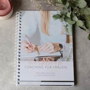 Könnte beinhalten: Ein weißes und graues Workbook mit dem Text "Workbook Coaching für Frauen" in rosa. Der Text darunter lautet "Finde heraus, wer du bist & was du wirklich willst!" und "Isabelle Hahn - Shemotion Coaching".