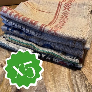 Könnte beinhalten: Ein Stapel von fünf Jutesäcken mit aufgedrucktem Text und Designs in Rot, Blau und Grün. Das Wort "ASSORTED" steht oben. Ein grüner Aufkleber mit "X5" befindet sich unten links. Die Säcke liegen auf einer Holzoberfläche.