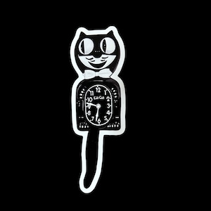 May include: A black and white Kit-Cat Klock in the shape of a cat. The clock has a white bow tie, a smiling face, and a pendulum tail. The clock face displays the time with black numbers and hands.