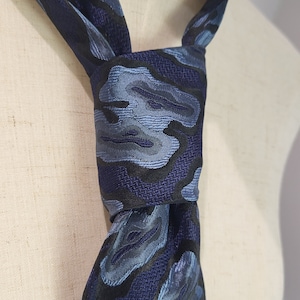 Peut inclure: Une cravate à motif bleu et noir avec un design camouflage. La cravate est nouée autour d'un mannequin blanc.