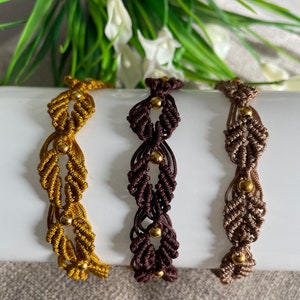 Puede incluir: Tres pulseras de macramé con cuentas doradas. Las pulseras son de color marrón, beige y amarillo mostaza.
