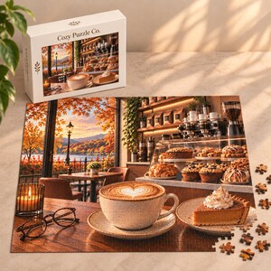 May include: A jigsaw puzzle box and completed puzzle featuring a cafe scene with a latte, a slice of pumpkin pie with whipped cream, and eyeglasses on a wooden table. The background shows a window view of an autumn lake, pastries, and coffee equipment.