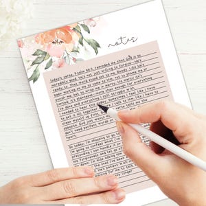May include: A handwritten notes page with floral accents. The page features lined sections with text, and the word "notes" at the top. A hand holding a pen is writing on the page.