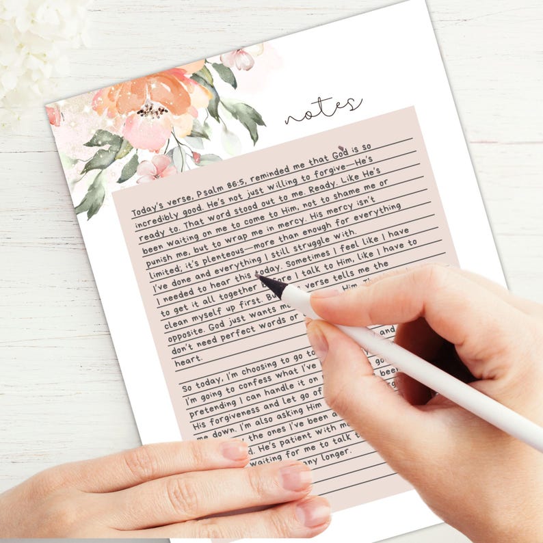 May include: A handwritten notes page with floral accents. The page features lined sections with text, and the word "notes" at the top. A hand holding a pen is writing on the page.