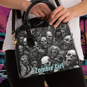 Puede incluir: Bolso de mano de cuero negro con un estampado gráfico de caras de zombis y el texto "Zombie Girl".