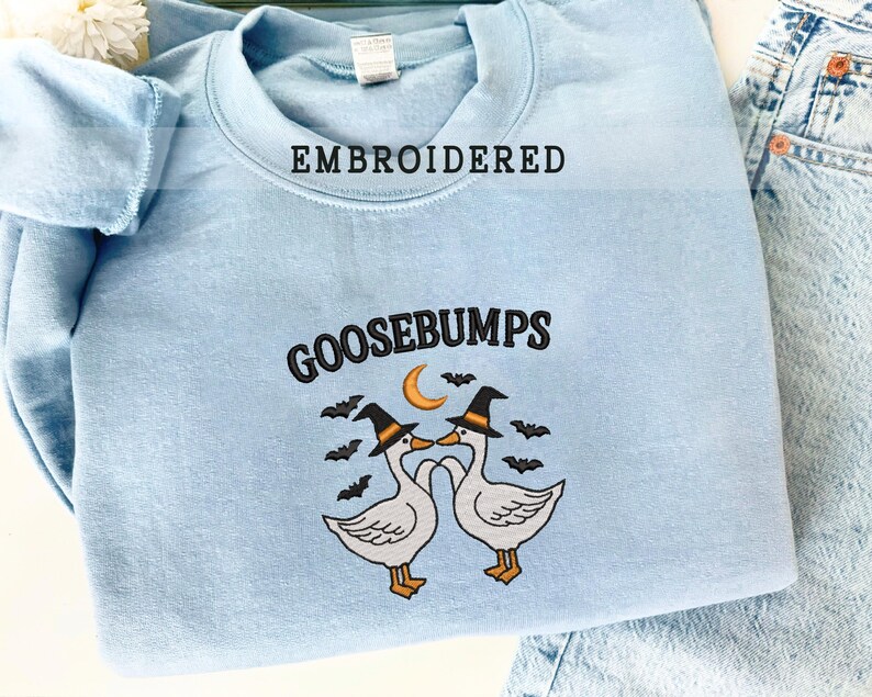 May include: Light blue embroidered sweatshirt with the word "GOOSEBUMPS" and a graphic of two geese wearing witch hats, a crescent moon, and bats. The word "EMBROIDERED" is embroidered above the collar.
