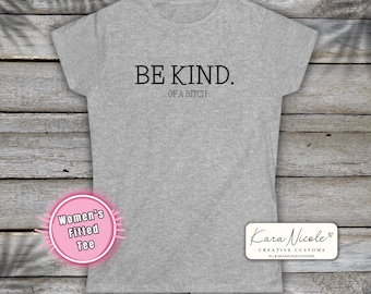 Könnte beinhalten: Ein meliertes graues T-Shirt mit dem schwarzen Aufdruck "BE KIND. OF A BITCH". Das T-Shirt hat einen Rundhalsausschnitt und kurze Ärmel. Ein rosa-weißer Aufkleber zeigt "Women's Fitted Tee". Ein weißes Rechteck mit dem Text "Kara Nicole CREATIVE CUSTOMS" ist ebenfalls sichtbar.