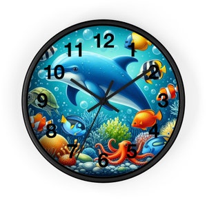 Op de afbeelding: Een zwarte geframed klok met een blauwe dolfijn, oranje, gele en rode vissen en een octopus in een koraalrif-omgeving. De wijzerplaat van de klok heeft zwarte cijfers van 1 tot en met 12.