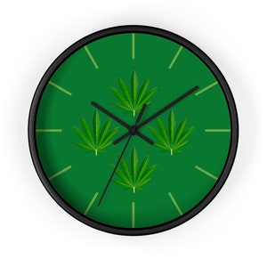 May include: Circular wall clock with a black frame and a green face. The clock face displays four green cannabis leaves and black clock hands. The background is a solid green colour, and the clock has light green hour markers.