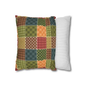 Puede incluir: Una almohada de patchwork con una variedad de colores y patrones, incluyendo verde, marrón, naranja, rojo y blanco. La almohada se combina con una almohada blanca con rayas grises.