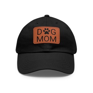 Peut inclure: Casquette de baseball noire avec un patch en cuir marron qui dit "DOG MOM" avec une empreinte de patte.