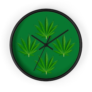 Op de afbeelding: Een groene wandklok met vier marihuanabladontwerpen op een groene achtergrond. De wijzers van de klok zijn zwart.