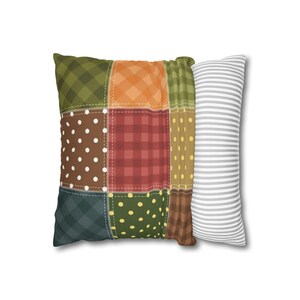Puede incluir: Una almohada de patchwork con una variedad de patrones, incluyendo cuadros verdes, cuadros naranjas, cuadros rojos, lunares marrones y lunares amarillos. La almohada está rodeada por una almohada blanca con rayas grises.