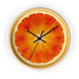 Op de afbeelding: Een ronde wandklok met een houten frame en een feloranje schijf fruit als wijzerplaat. De wijzers van de klok zijn zwart.