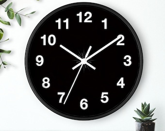 May include: A black clock with white numbers and hands on a white wall. The clock is round and has a black frame.