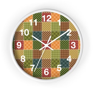 May include: A round wall clock with a white frame. The clock face features a patchwork design in various colors, including green, orange, brown, and red. White numerals mark the hours, and white hands indicate the time.