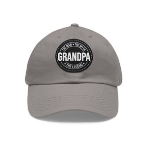 Peut inclure: Casquette de baseball grise avec un patch circulaire noir et blanc qui dit "The Man The Myth Grandpa The Legend".