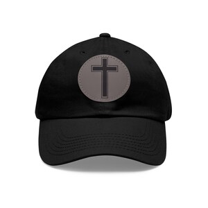 Peut inclure: Casquette de baseball noire avec un patch circulaire gris orné d'une croix noire.