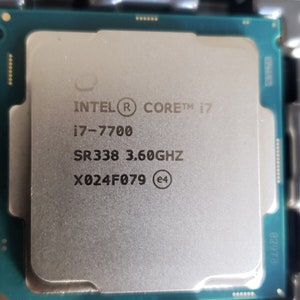 Puede incluir: Primer plano de un procesador Intel Core i7-7700. La CPU plateada tiene el logotipo de Intel y la información del modelo impresos en su superficie. El procesador está montado en una placa de circuito verde con puntos de contacto dorados.