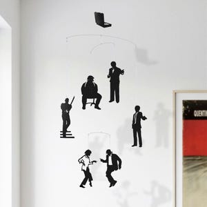 May include: A black mobile featuring six figures of characters from the film Pulp Fiction. The figures are suspended from a metal frame and are silhouetted against a white background.
