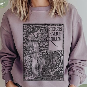 May include: A mauve-colored sweatshirt featuring a black and white illustration from Spenser's Faerie Queene. The design includes a woman, a lion, and floral elements. The text "SPENSER'S FAERIE QUEENE" is displayed on a banner. The sweatshirt has a crew neck and long sleeves.
