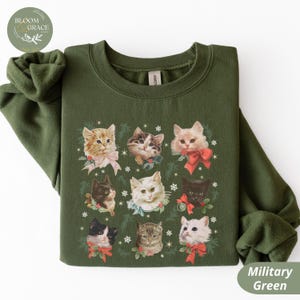 Peut inclure: Sweat-shirt vert militaire avec un motif festif de neuf chats avec des n&oelig;uds et de la verdure. Les chats sont de diff&eacute;rentes couleurs, dont orange, noir et blanc. Le sweat-shirt a un col rond et des manches longues.