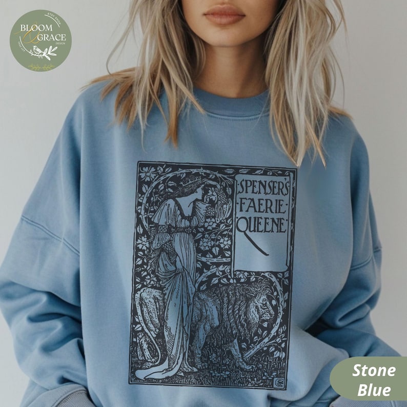 Puede incluir: Sudadera azul piedra con una ilustraci&oacute;n en blanco y negro que representa a una mujer, un le&oacute;n y el texto "SPENSERS FAERIE QUEENE". La sudadera tiene mangas largas y cuello redondo.