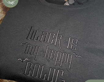 May include: Black sweatshirt with embroidered text that reads "Black is my happy color." The sweatshirt has a crew neck and long sleeves. The text is in a gothic style font. The word "Black" is also written on a green label.