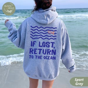 May include: Sport grey hoodie with a blue and orange graphic on the back. The graphic features wavy lines, a fish, and the text "IF LOST, RETURN TO THE OCEAN". The hoodie is shown on a person at the beach.