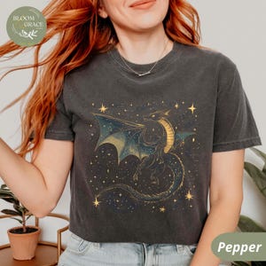 May include: A dark gray t-shirt featuring a detailed illustration of a dragon with gold and blue accents, set against a starry background. The shirt has the word "Pepper" printed on it.