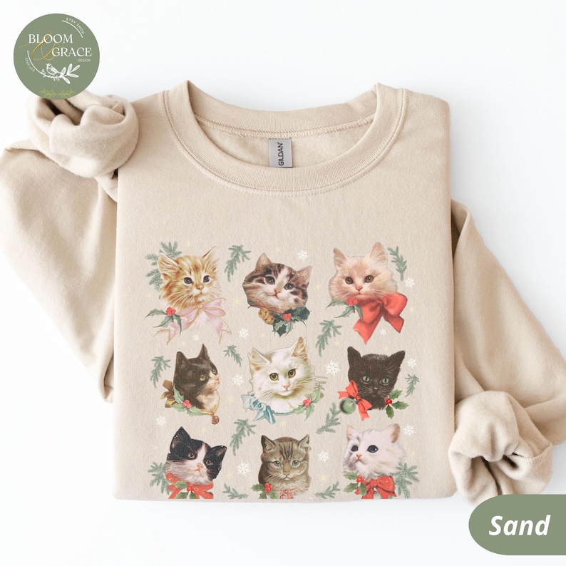 Peut inclure: Sweat-shirt couleur sable avec un motif de neuf chats, chacun orn&eacute; de n&oelig;uds et de verdure festifs. Les chats sont de diff&eacute;rentes couleurs et motifs, cr&eacute;ant un design charmant sur le th&egrave;me des f&ecirc;tes. Le sweat-shirt a un col rond et des manches longues.