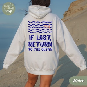 May include: White hoodie with blue text that reads "IF LOST, RETURN TO THE OCEAN." The back of the hoodie features a blue wave design with a small orange fish. The hoodie is a comfortable, casual style.