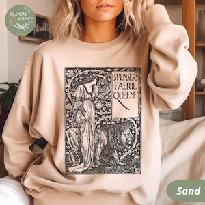 Puede incluir: Sudadera color arena con una ilustraci&oacute;n en blanco y negro de "Spensers Faerie Queene". El dise&ntilde;o incluye una mujer, un le&oacute;n y elementos florales. La sudadera tiene cuello redondo y mangas largas.