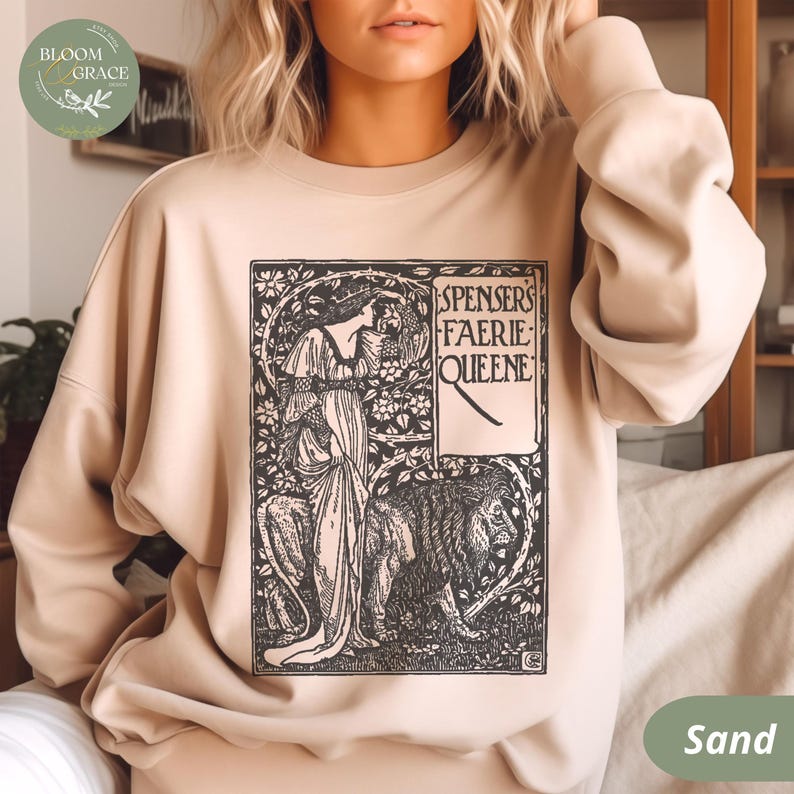 Puede incluir: Sudadera color arena con una ilustraci&oacute;n en blanco y negro de "Spensers Faerie Queene". El dise&ntilde;o incluye una mujer, un le&oacute;n y elementos florales. La sudadera tiene cuello redondo y mangas largas.