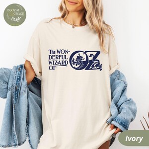 May include: A white t-shirt featuring a navy blue graphic of the text "The Wonderful Wizard of Oz" and a lion with a crown. The graphic is in a vintage style.