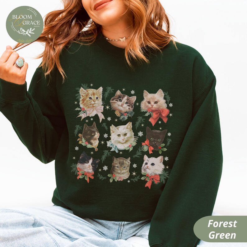 Peut inclure: Sweat-shirt vert for&ecirc;t orn&eacute; d'une grille de neuf portraits de chats, chacun orn&eacute; de n&oelig;uds et de verdure festifs. Les chats varient en couleur et en motif, sur fond de flocons de neige. Le sweat-shirt a un col rond et des manches longues.