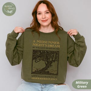 Puede incluir: Sudadera verde militar con el texto "A Midsummer Night's Dream" de William Shakespeare, con ilustraciones de Arthur Rackham. El diseño incluye una ilustración de árbol de estilo vintage. La sudadera es de color liso.