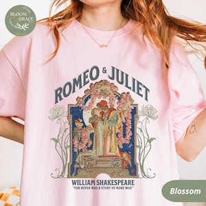 Puede incluir: Camiseta rosa claro con la inscripción "ROMEO & JULIET" y una ilustración de los personajes de la obra. La camiseta también incluye el texto "WILLIAM SHAKESPEARE" y la cita "FOR NEVER WAS A STORY OF MORE WOE".